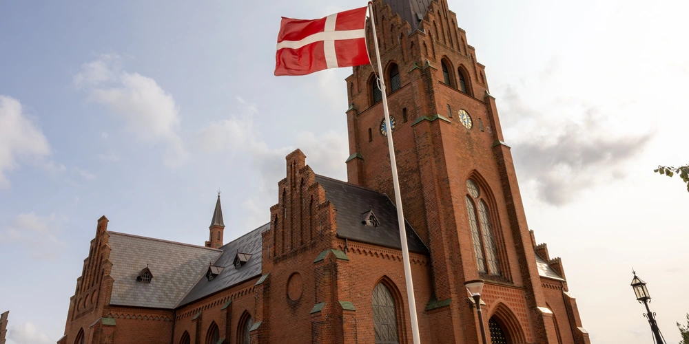 Rote Backsteinkirche mit dänischer Flagge vor weißem Himmel.