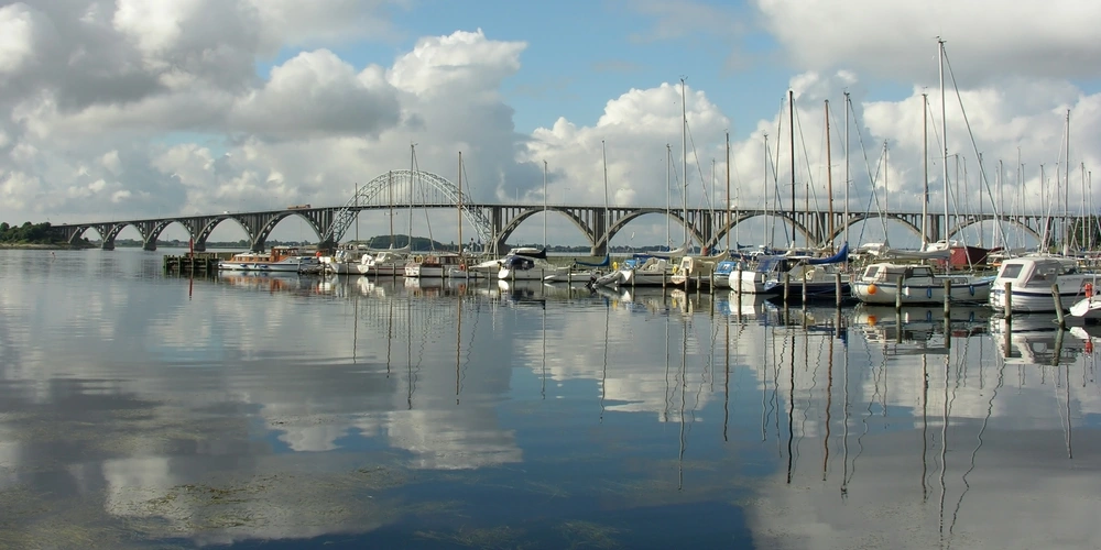 Eine Brücke über einen ruhigen Wasserweg, umgeben von Booten und Wolken.