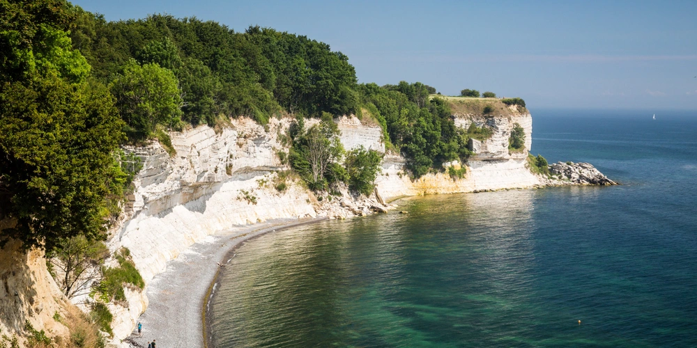 Küstenlandschaft mit weißen Klippen und ruhigem Wasser unter blauem Himmel.