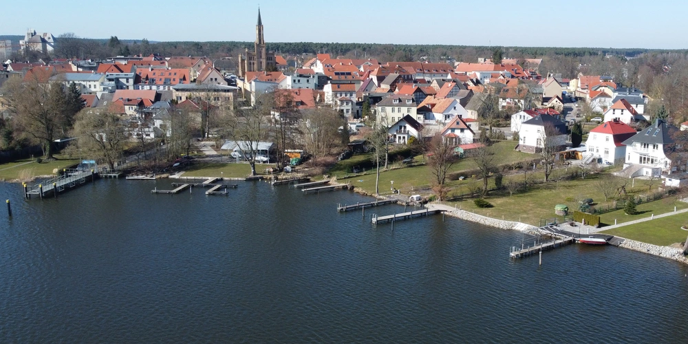 Luftaufnahme eines Dorfes am Wasser mit roten Dächern und grünen Flächen.