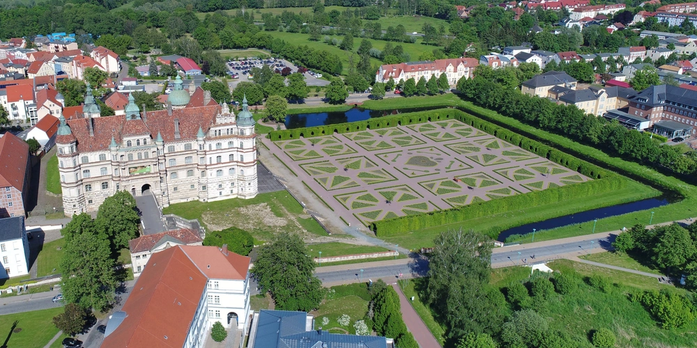 Luftaufnahme eines Schlosses mit symmetrischem Park und grünen Landschaften.