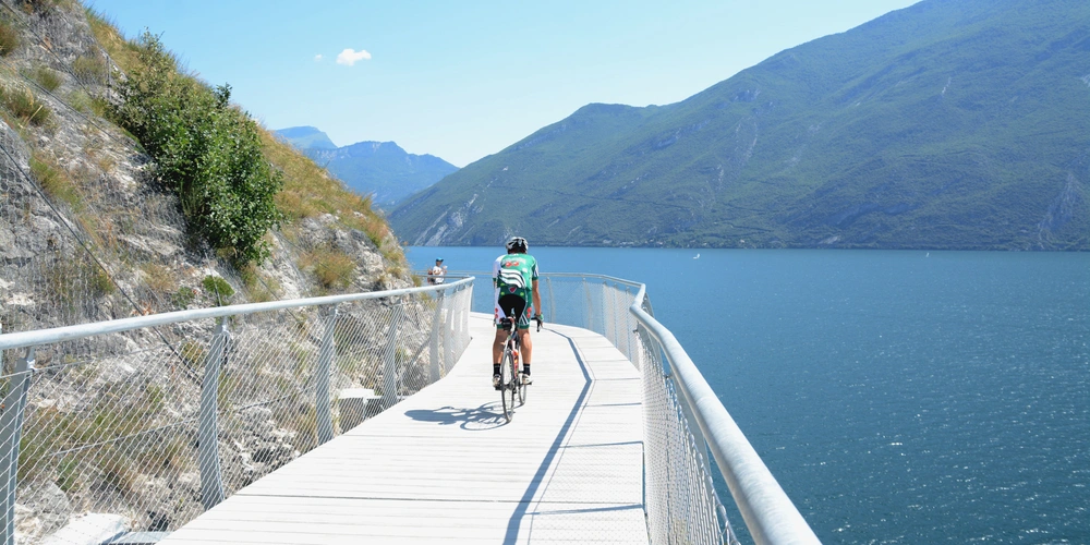 Fahrradfahrer auf einer Holzbrücke mit Blick auf den blauen See und die Berge.
