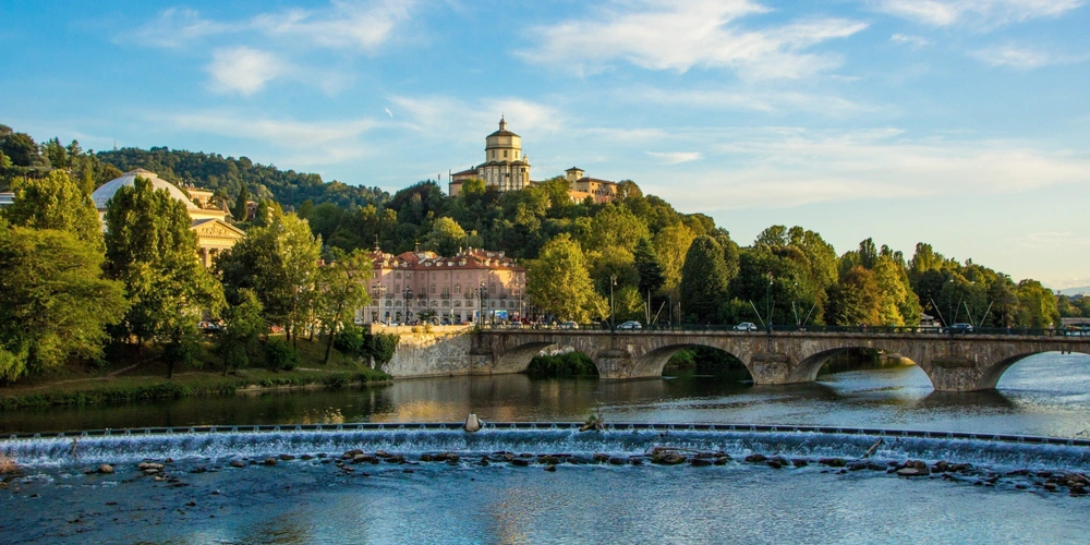 Panoramablick auf einen Fluss, Brücke und Hügel mit Bäumen und historischem Gebäude.