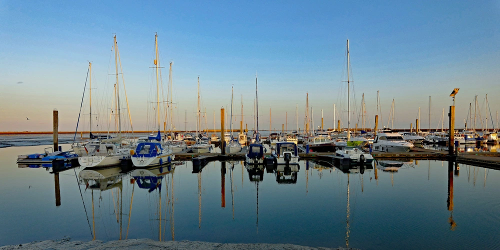 Hafen mit Booten und Spiegelung im Wasser, blauer Himmel im Hintergrund.