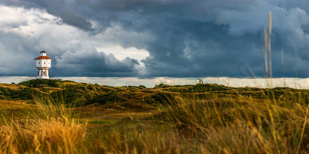 Leuchtturm im Grünen unter einer dunklen, bewölkten Himmelstimmung.