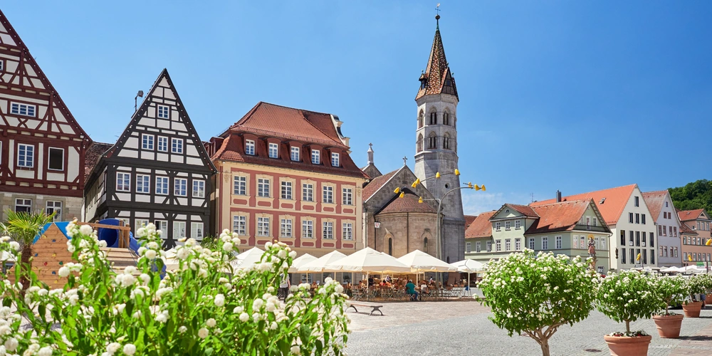 Lebhafte Stadtansicht mit Fachwerkhäusern, Kirche und blühenden Blumenbäumen.
