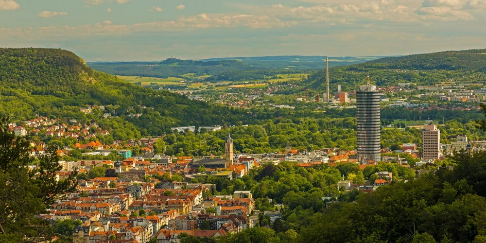 Blick auf eine Stadtlandschaft mit grünen Hügeln und modernen Gebäuden.