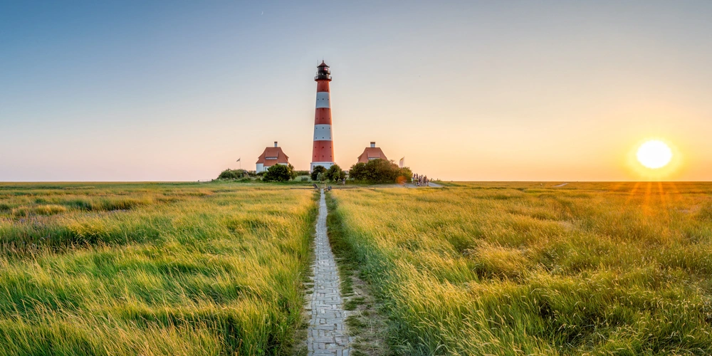 Leuchtturm in einer grünen Wiese bei Sonnenuntergang, warmes Licht strahlt.