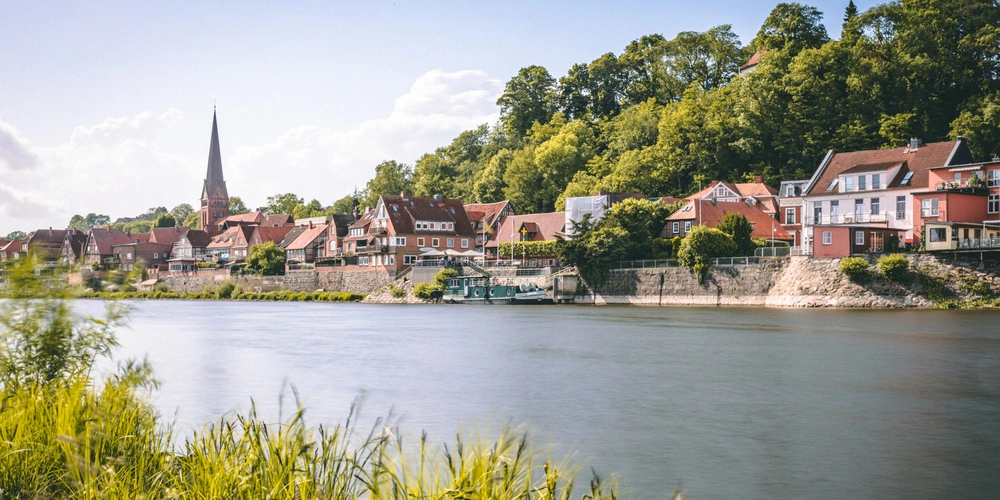 Idyllische Uferlandschaft mit Häusern, Kirche und grünen Bäumen am Flussufer.