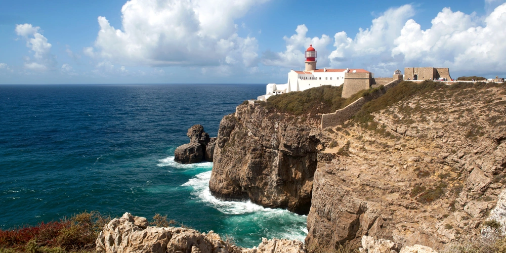 Leuchtturm auf einer Klippe mit Blick auf den Ozean und bewölkten Himmel.