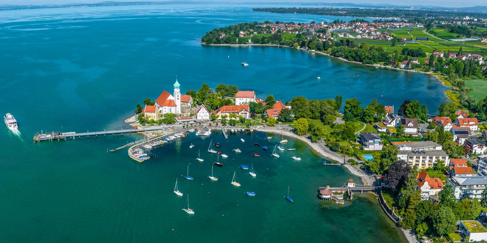 Luftaufnahme eines malerischen Hafenorts am Wasser mit Booten und grüner Landschaft.