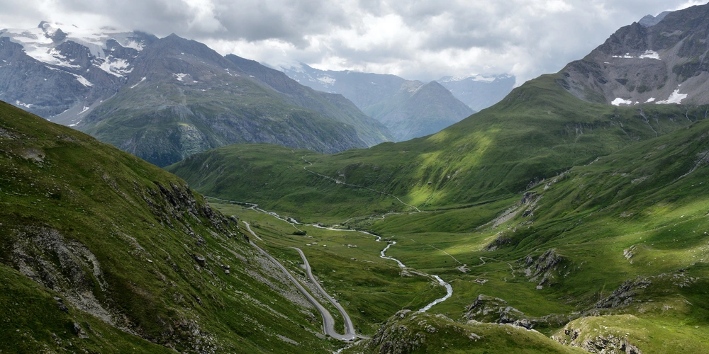 Grüne Berglandschaft mit einem Serpentinenweg und Wolken am Himmel.