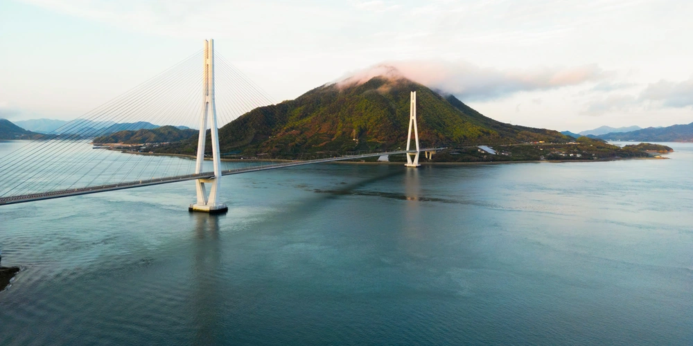 Blick auf eine Brücke, die eine Insel mit Hügeln über Wasser verbindet.