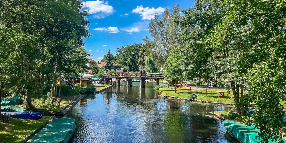 Ein ruhiger Fluss mit Booten, umgeben von Bäumen und einem blauen Himmel.