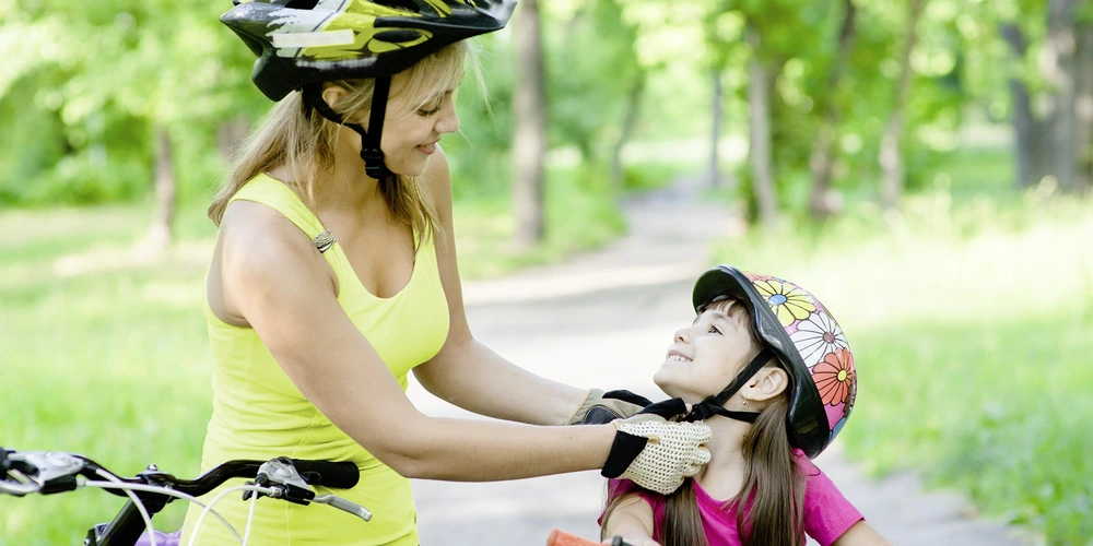 Tipps & Tricks Frau befestigt den Fahrradhelm eines Kindes