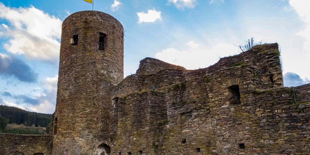 Teilweise ruinierte Burg mit rundem Turm und blauem Himmel im Hintergrund.