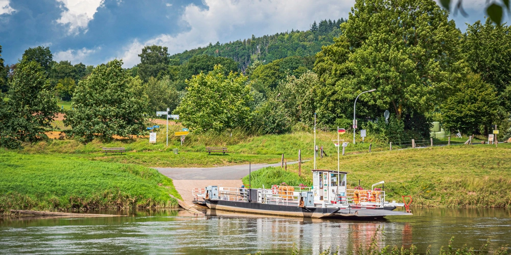 Die Fähre Lippoldsberg liegt am Ufer, umgeben von grünen Bäumen und Hügeln