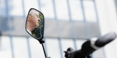 Fahrradrückspiegel mit reflektierenden Fenstern und einem weißen Helm im Hintergrund.