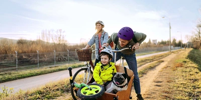 Fröhliche Familienradtour mit Fahrrad und Lastenrad mit Kind und Hund im Anhänger 