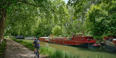 Radfahrer fährt am Canal du Midi in Frankreich entlang, auf dem Boote liegen.