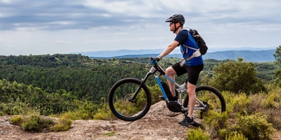 Mann auf einem E-Mountainbike steht auf der Spitze eines Berges.