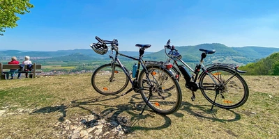 Zwei Fahrräder stehen während einer Radtour auf einer Wiese mit Blick auf grüne Hügel und blauen Himmel