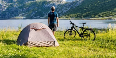 Mann macht Urlaub mit Zelt und Fahrrad am Seeufer in der Natur