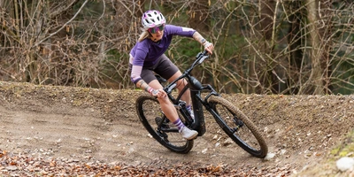 Mountainbikerin fährt mit Schwung eine kurvige Strecke im Wald.
