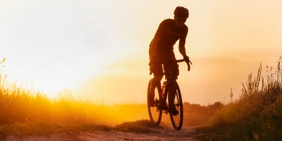 Cyclocross vs. Gravel: Unterschiede der Offroad-Bikes Radfahrer bei Sonnenuntergang auf einem staubigen Weg.
