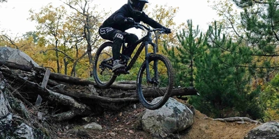 Wir haben für dich die besten Downhill Strecken in Deutschland zusammengesucht. Frau fährt mit Mountainbike durch Wald einen Abhang hinunter.