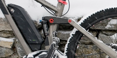 Ein E-Bike mit Schnee und Steinmauer im Hintergrund, Fokus auf dem Antriebssystem.