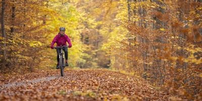 E-Bike-Akku-Lebensdauer Frau fährt auf dem Fahrrad durch den herbstlichen Wald