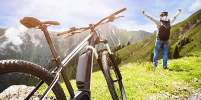 Person steht mit dem Rücken zum Betrachter auf einer grünen Wiese und hebt die arme. Das E-Bike steht im Vordergrund.