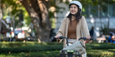 E-Bike für Damen Testsieger: Finde das beste Damen Pedelec im Test Junge Frau mit Helm auf einem Fahrrad in einem Park, lächelt zufrieden.