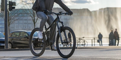E-Bike Trekking Testsieger: Die besten Trekking E-Bikes Radfahrer in urbaner Umgebung, vorbei an einem Wasserfall und Fußgängern.