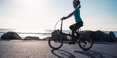 Frau fährt auf einem Klapprad am Meer entlang