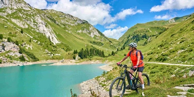 Frau steht auf Crossbike neben See zwischen Bergen.