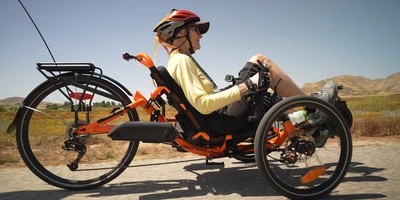 Elektro Dreirad Testsieger: Die besten Modelle im Test Eine Person sitzt in einem bunten Dreirad auf einem Radweg, umgeben von Landschaft.