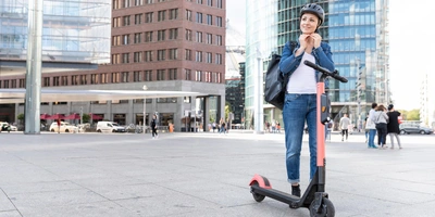 Frau steht neben E-Scooter und setzt sich einen Helm auf.