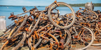 So entsorgst du dein Rad richtig Ein Haufen rostiger Fahrradrahmen und Räder am Ufer eines Gewässers.