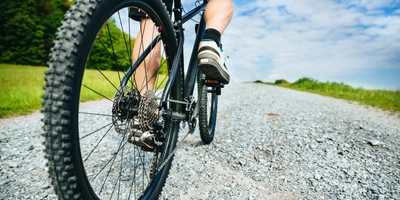 Dein Fahrrad-Hinterrad wackelt? Dann bist du hier richtig! Nahaufnahme eines Fahrradreifens auf einem Schotterweg unter blauem Himmel.