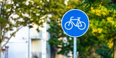 Blaues Verkehrsschild mit Fahrradsymbol vor grünen Bäumen.