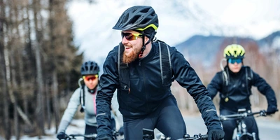So bleibst du auch im Winter mit deinem E-Bike sicher unterwegs. drei Fahrradfahrer mit Helm fahren im Winter auf Straße.