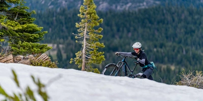 10 Tipps zum E-Bike fahren im Winter. Frau schiebt Mountainbike verschneiten Berg hoch.
