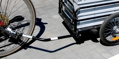 Fahrradanhänger mit Verbindung zu einem Fahrrad auf Pflastersteinen.