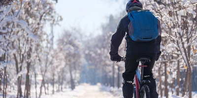Ein Radfahrer fährt auf einem verschneiten Weg zwischen Bäumen.