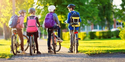mehrere Kinder mit Rucksack auf dem Fahrrad im Park
