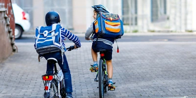 die richtige Größenwahl ist entscheidend zwei Kinder fahren mit Helm und Rucksack zur Schule