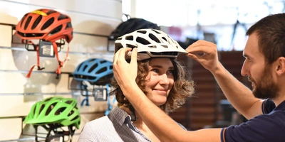 Frau wird von Fachhändler beraten und probiert im Geschäft verschiedene Fahrradhelme an.