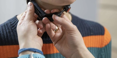 Eine Person überprüft bei einer Fahrradhelmträgerin, ob die Riemen den Hals nicht einengen.